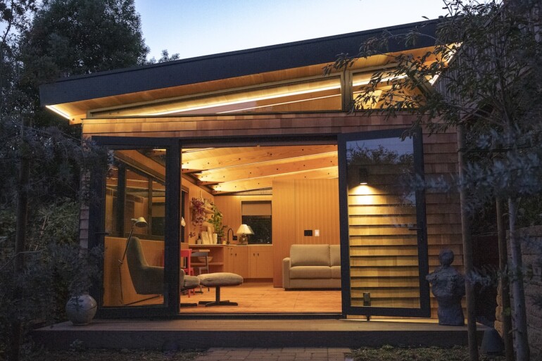 Modern cedar-clad ADU with large glass sliding doors, warm interior lighting, and outdoor deck at twilight in San Jose