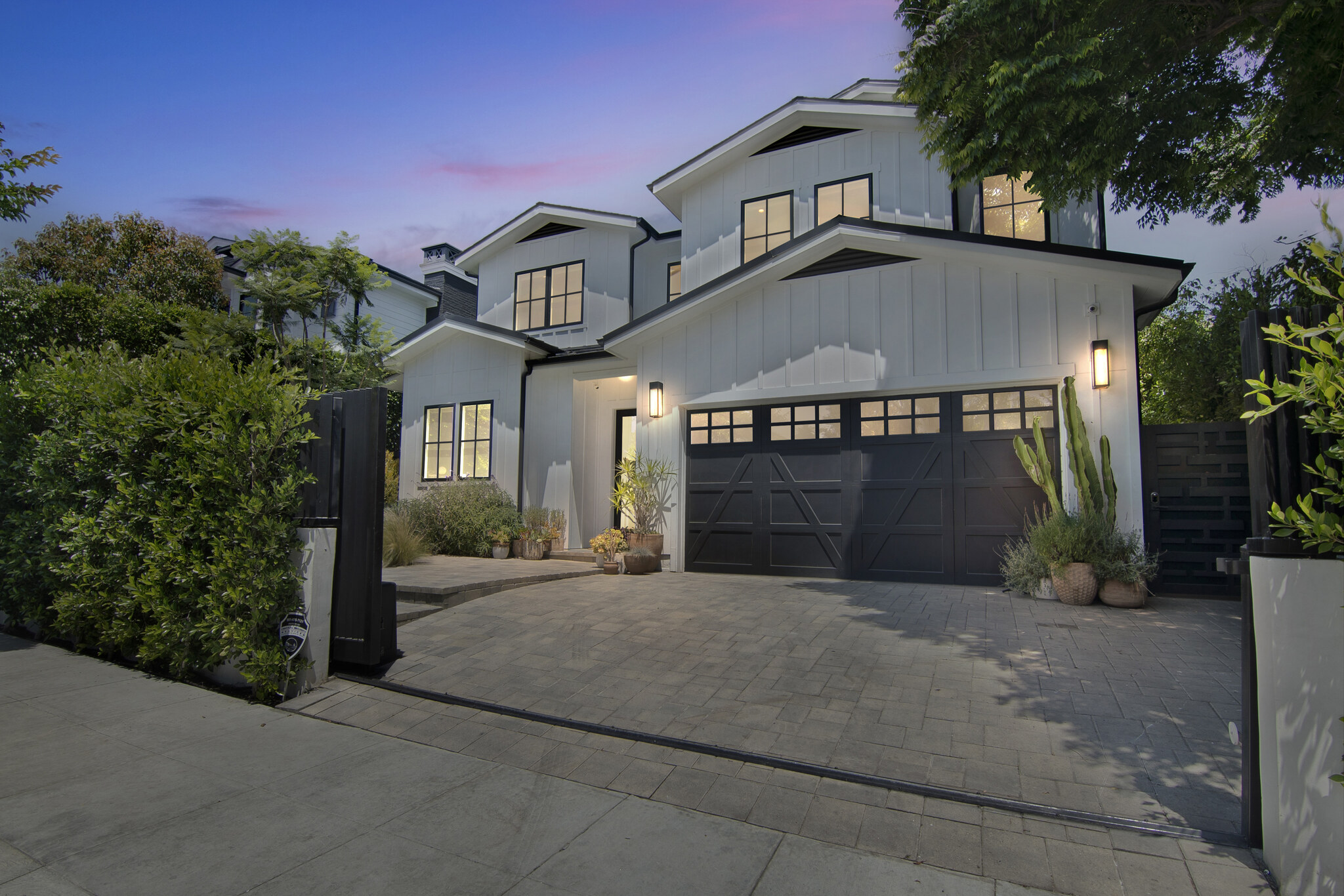 Dusk exterior, white farmhouse with black garage doors