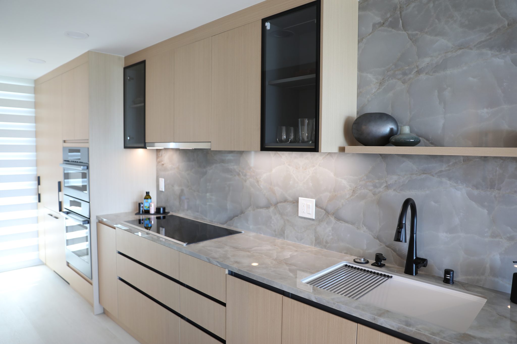 North Point kitchen with light oak cabinets, grey stone counters, and a full slab backsplash