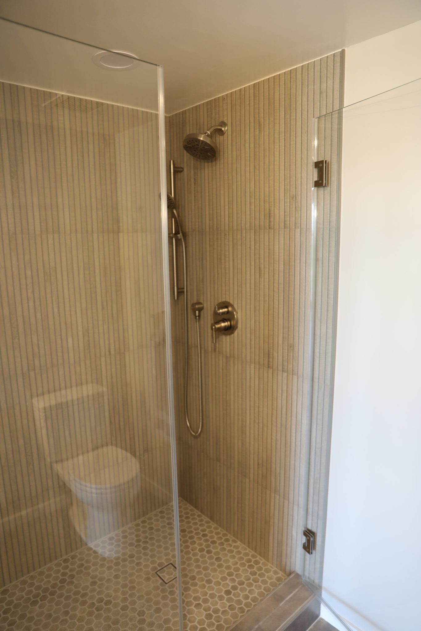 Glass shower with linear tile and brass fixtures