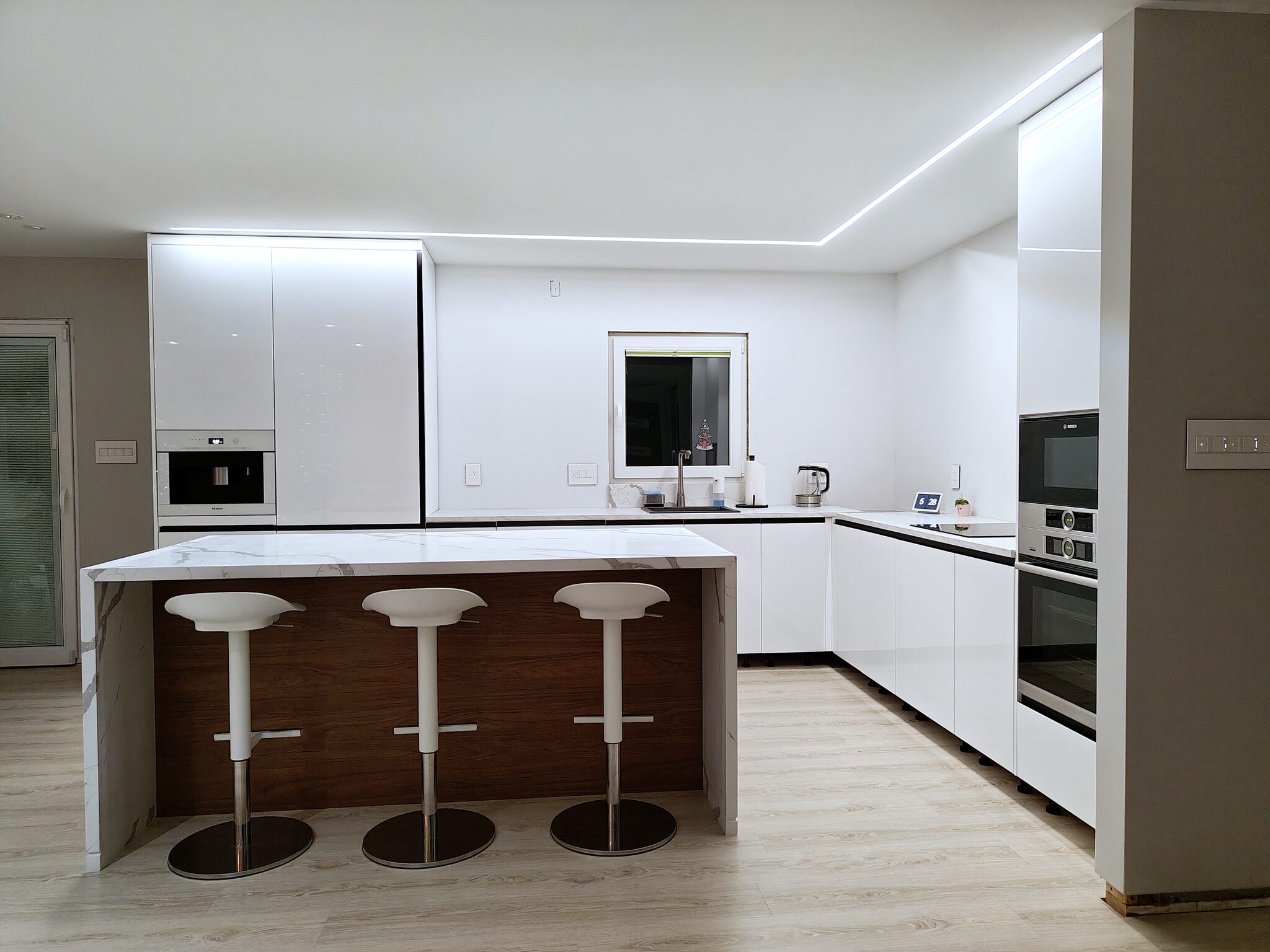 Kitchen with marble island, white cabinets, and cove lighting